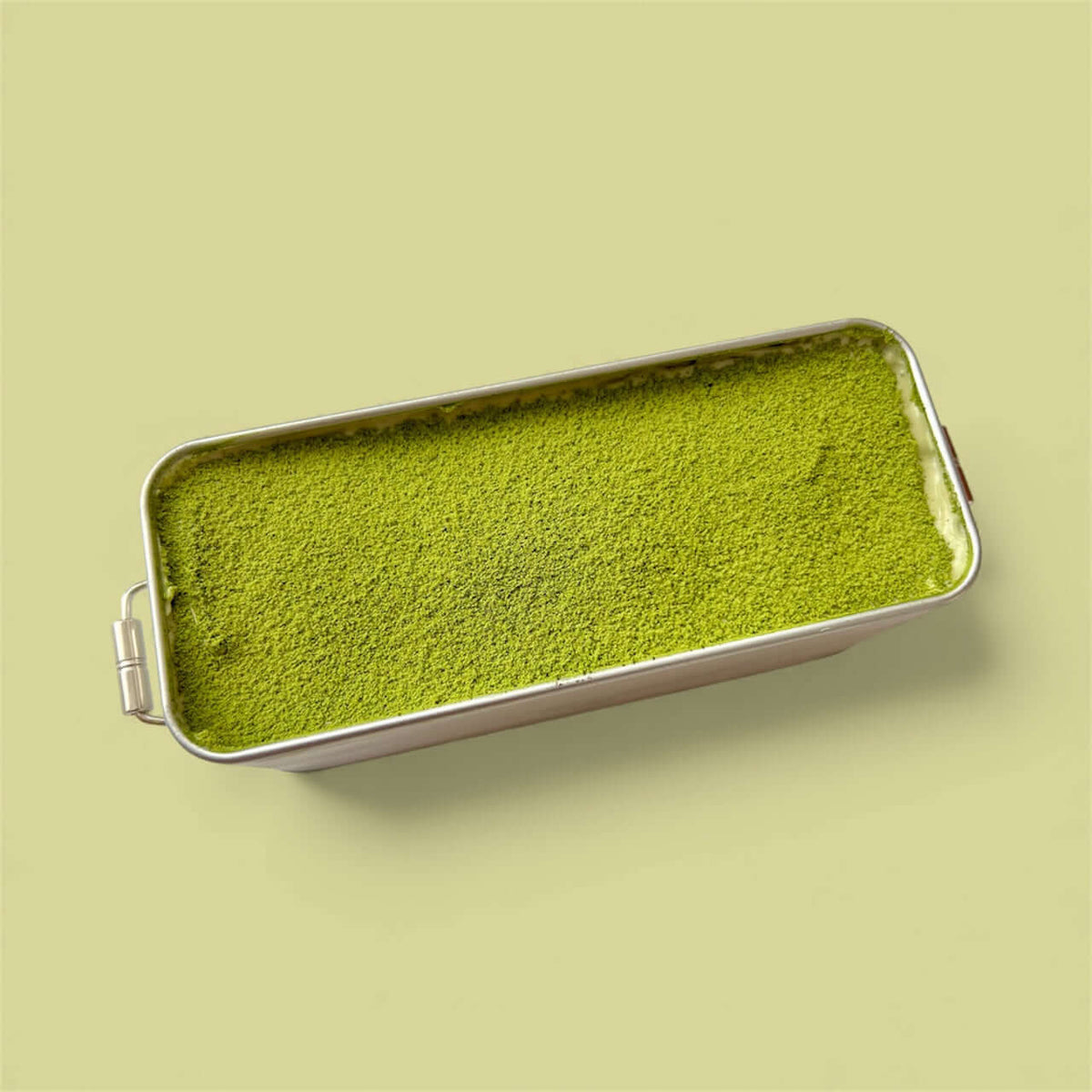 Classic Matcha Tiramisu in a silver tin, showcasing a vibrant green matcha layer on top.