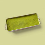 Classic Matcha Tiramisu in a silver tin, showcasing a vibrant green matcha layer on top.