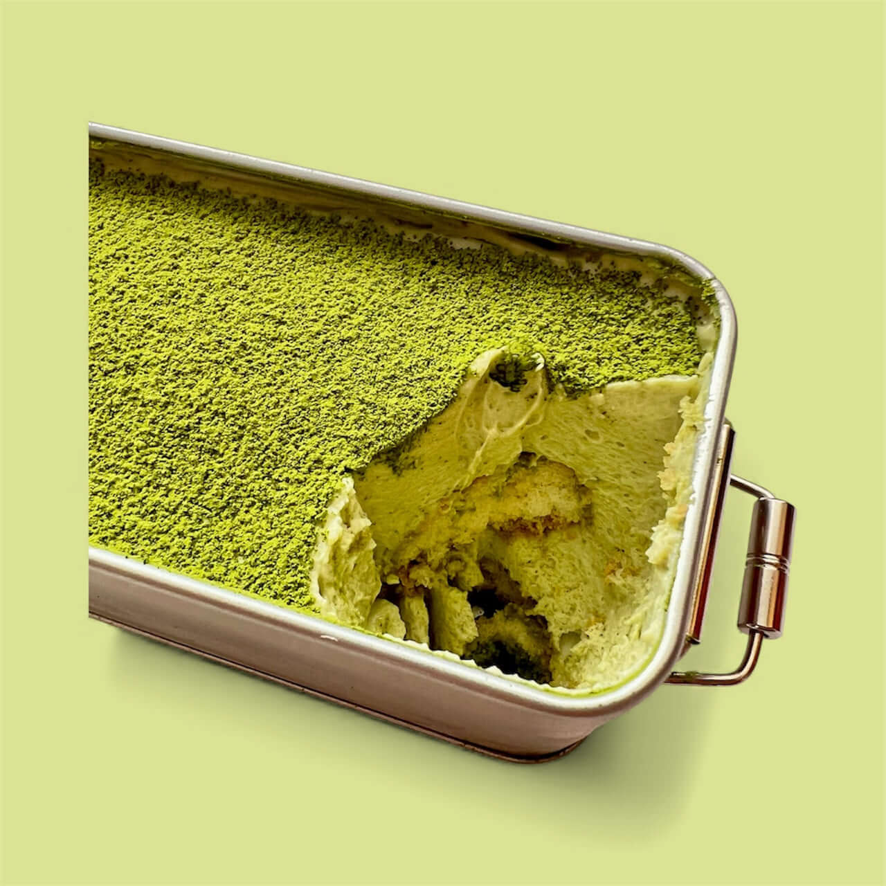 Close-up of Pistachio Matcha Tiramisu with one serving taken, showcasing vibrant green layers.
